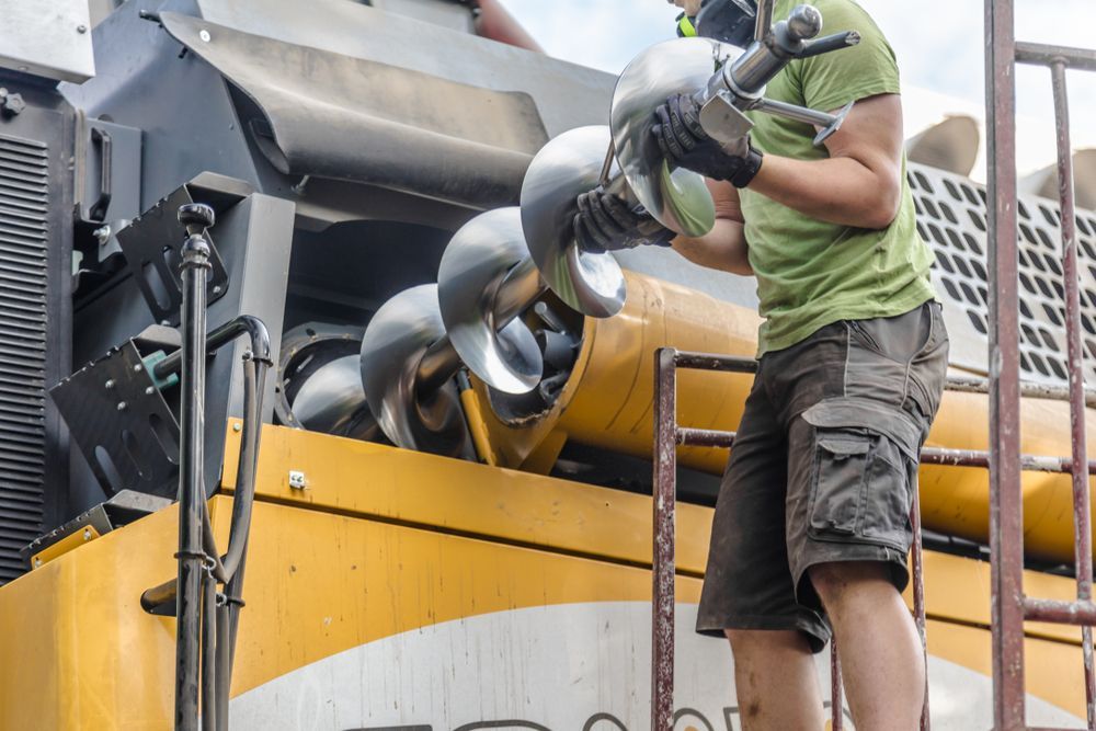 A Worker in a Green Shirt Installing a Metal Auger Component — Aspire Diesel In Dingo, QLD