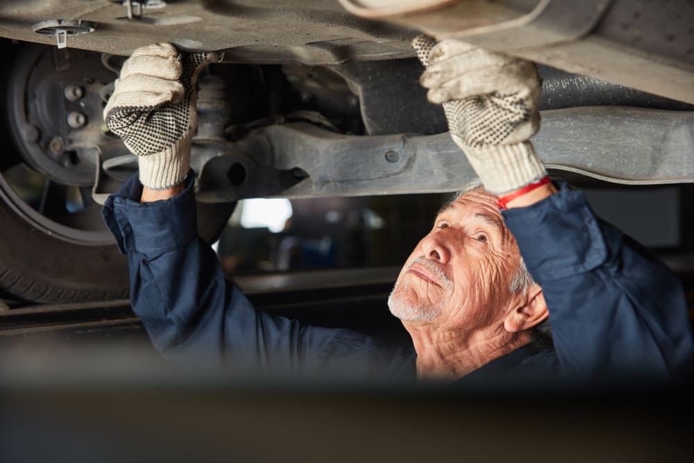 An Older Man Is Working Under A Car In A Garage — Aspire Diesel In Rockhampton, QLD