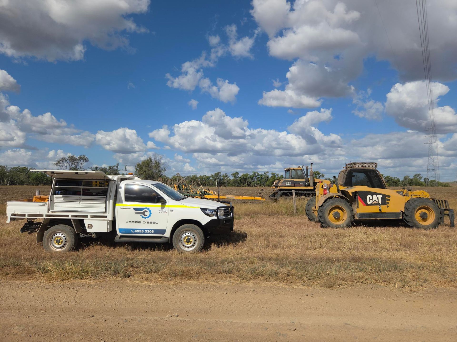 White utility truck and yellow CAT loader on a dirt field under a cloudy blue sky - Aspire Diesel In Gracemere, QLD