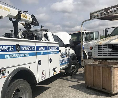 A white service truck with diagnostics and repair branding parked next to a white truck with its hood open for repairs.