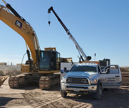 A yellow Caterpillar excavator sits next to a white service truck with a crane parked on a dirt construction site.