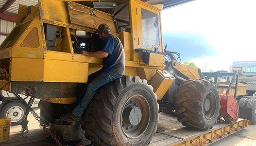 A man is working on a yellow tractor in a garage.