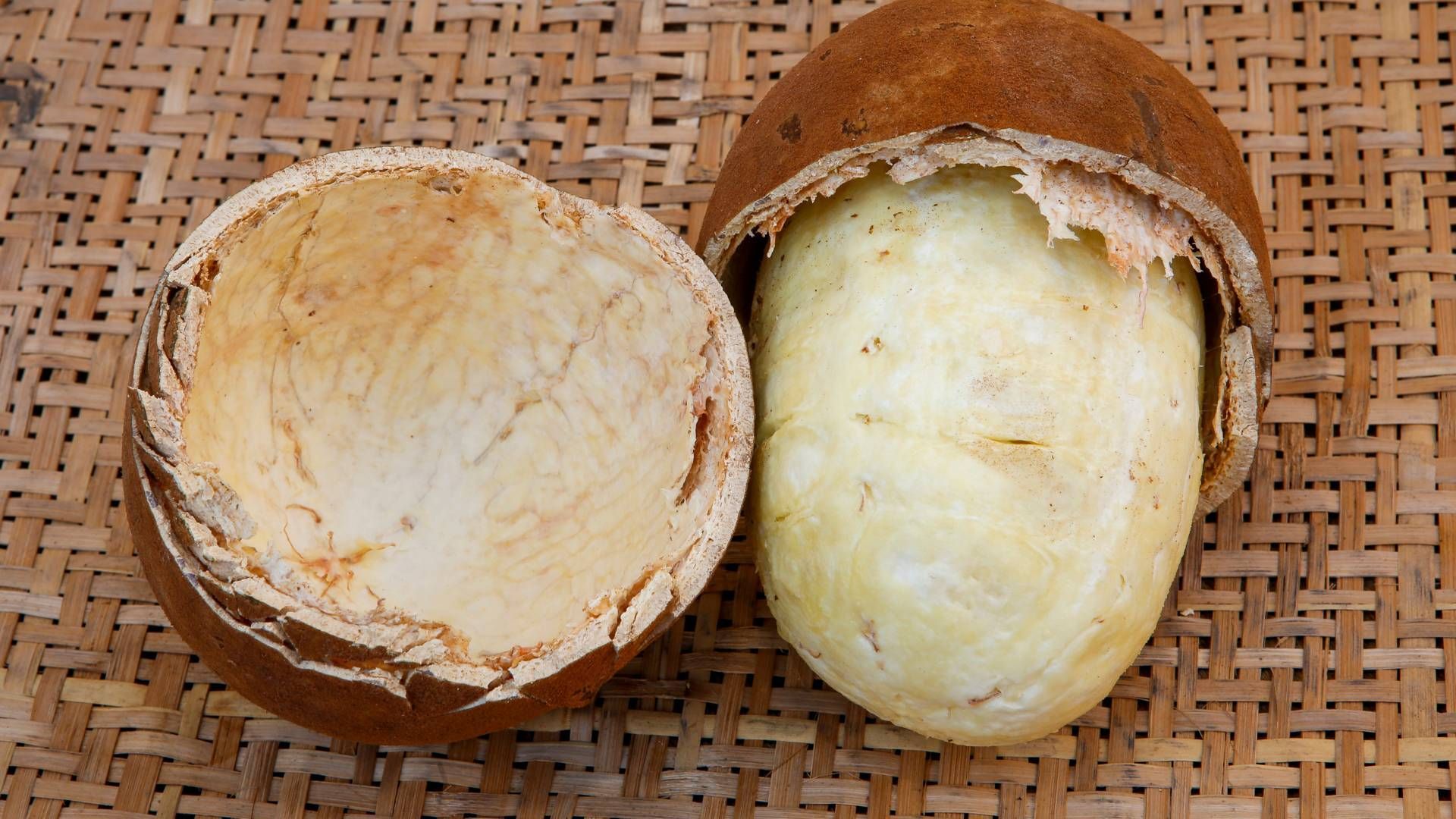 Um coco é cortado ao meio em uma superfície de vime