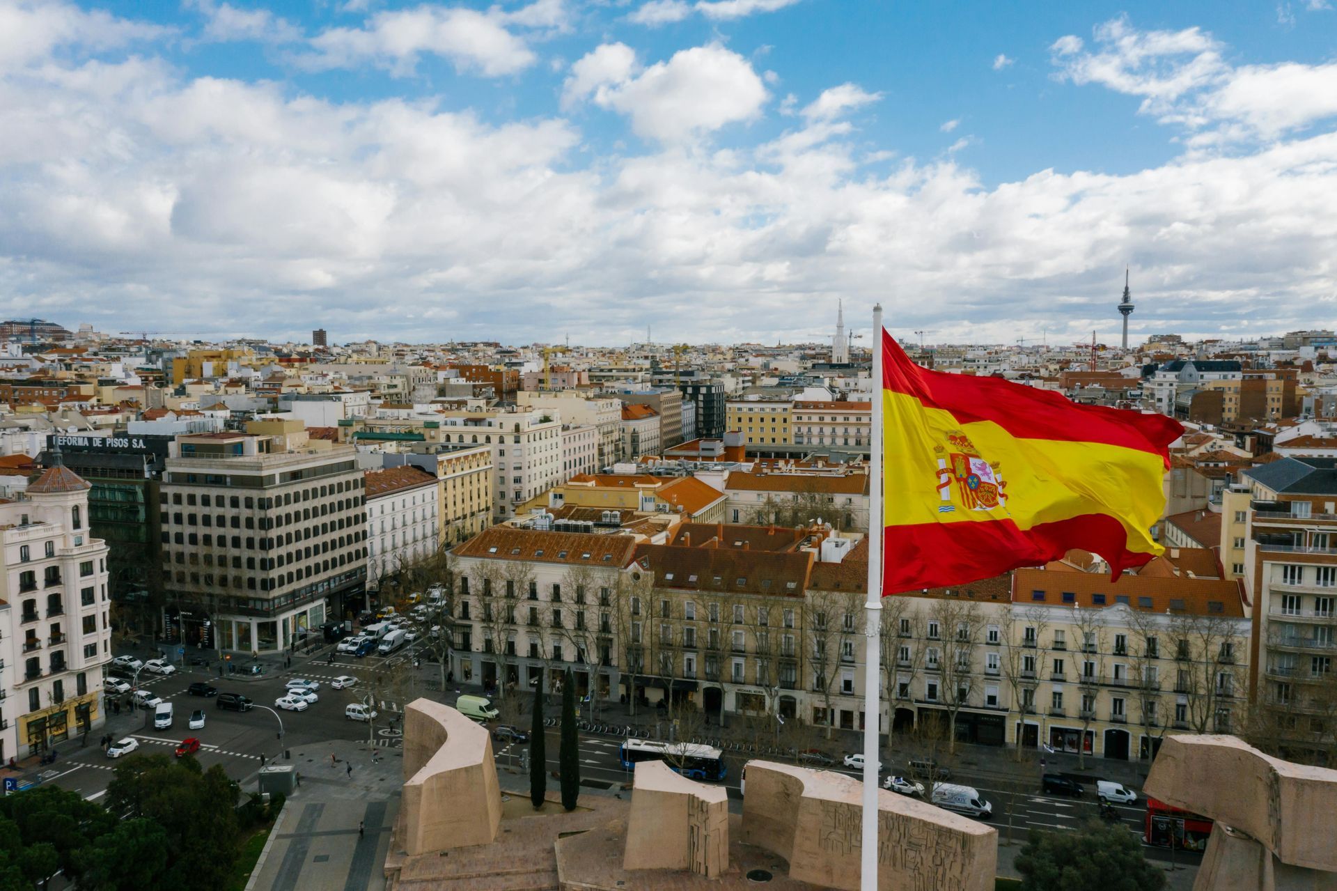 Spanish flag waving over Madrid cityscape, cloudy sky.