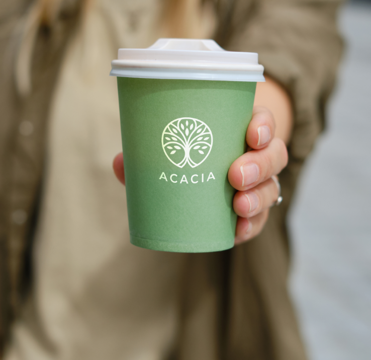 Een persoon houdt een groene beker vast met de tekst acacia