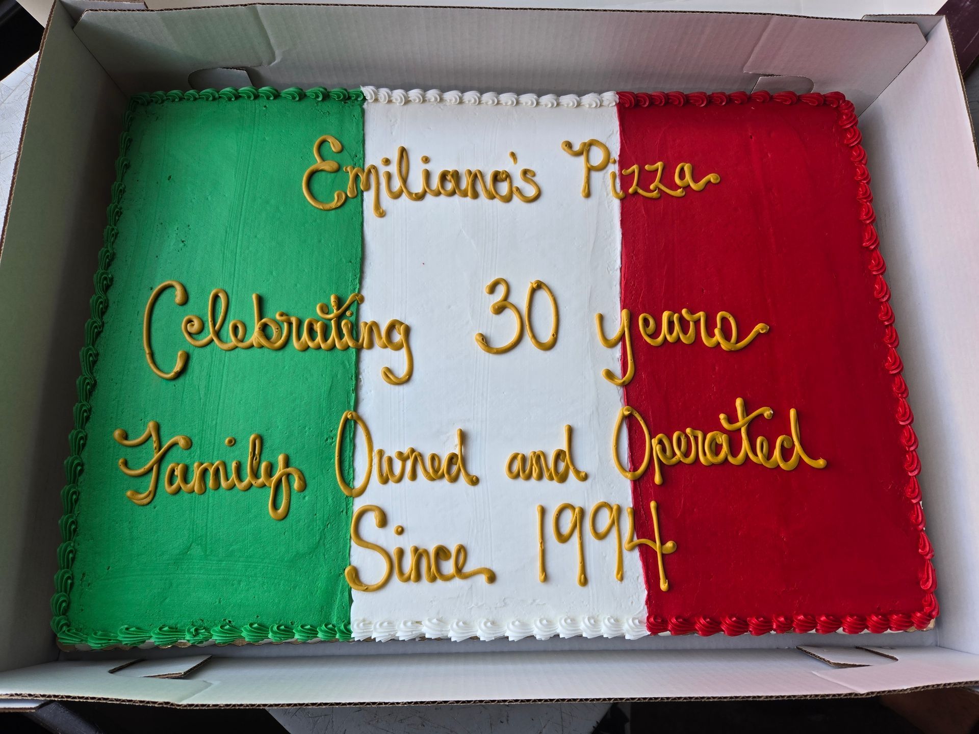 A cake in a box that says emiliano 's pizza celebrating 30 years family owned and operated since 1994