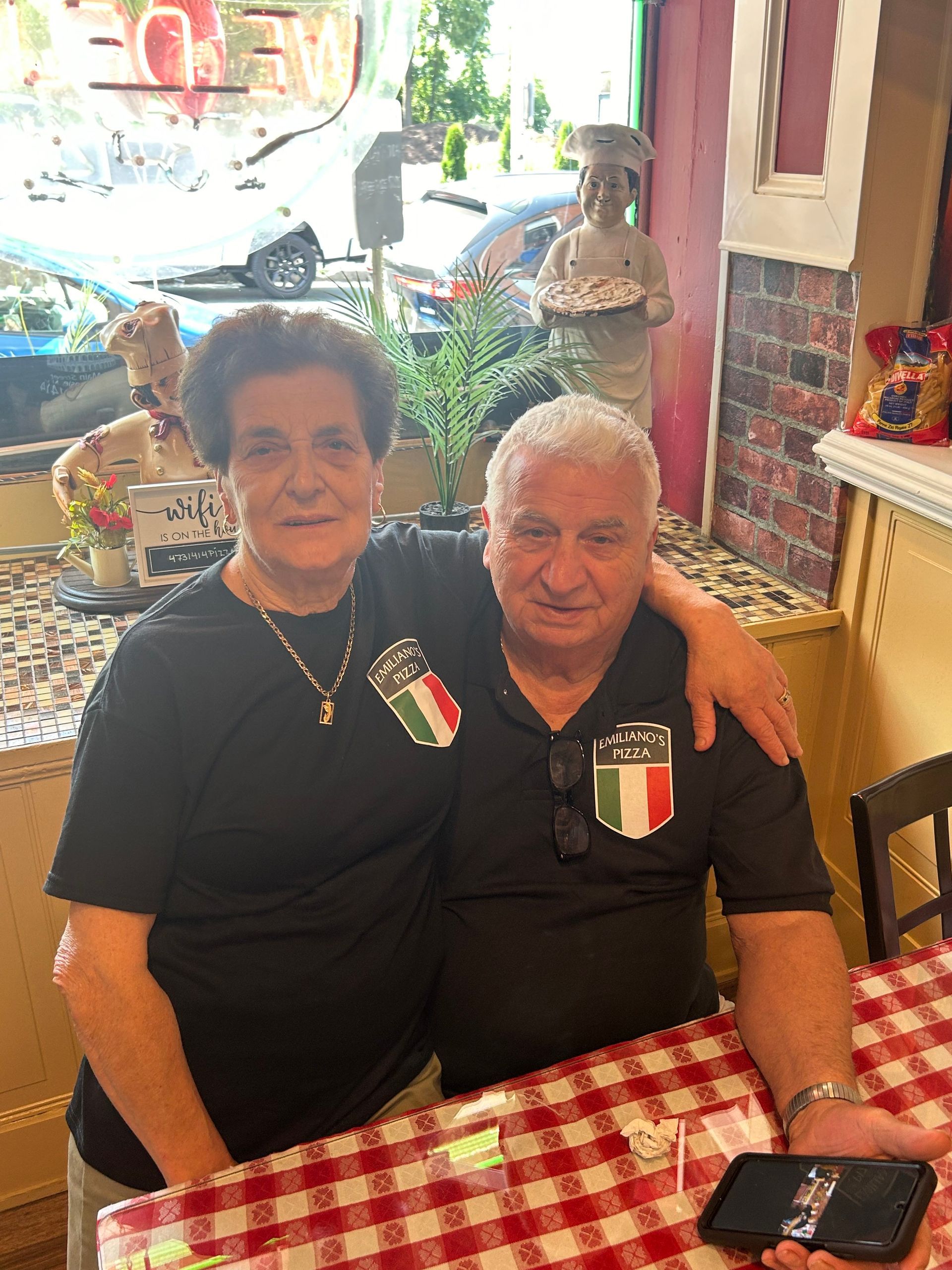 A man and a woman are sitting at a table with their arms around each other.