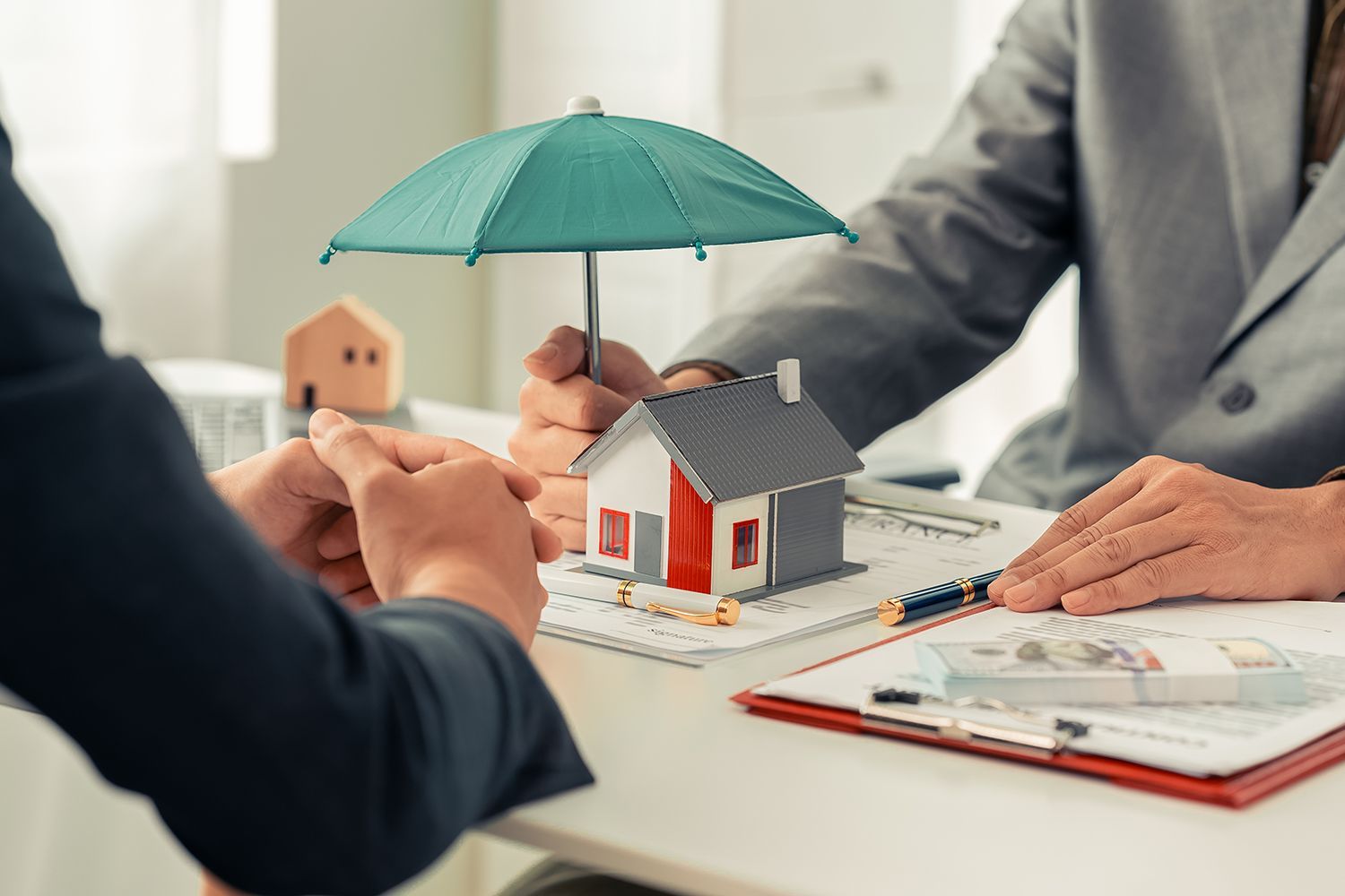 Hands holding a toy house under a small umbrella on a table with documents. Hands holding a toy house under a small umbrella on a table with documents.