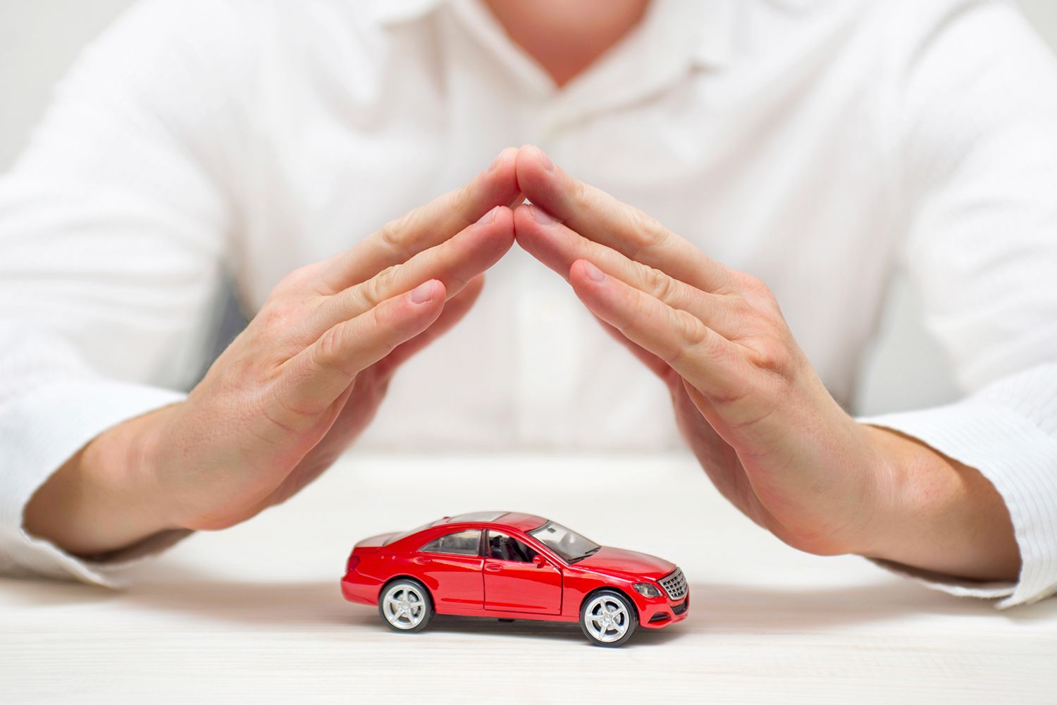 Hands over a red toy car, forming a protective roof, implying insurance or protection. Hands over a red toy car, forming a protective roof, implying insurance or protection.