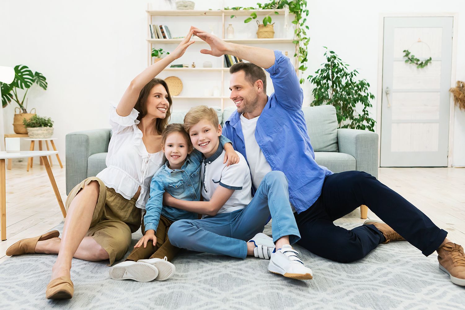 Family making a roof shape with their arms indoors, smiling, on a rug. Family making a roof shape with their arms indoors, smiling, on a rug.