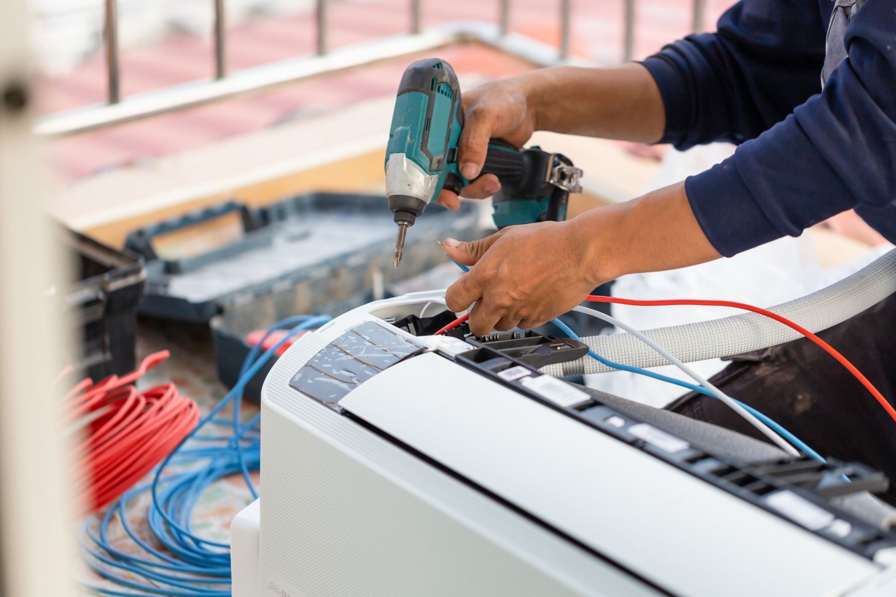 A man is fixing an air conditioner with a drill.