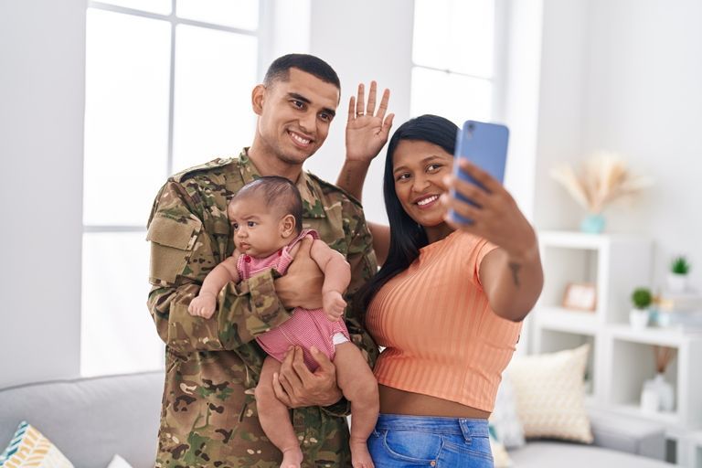 A soldier is taking a selfie with his wife and baby.