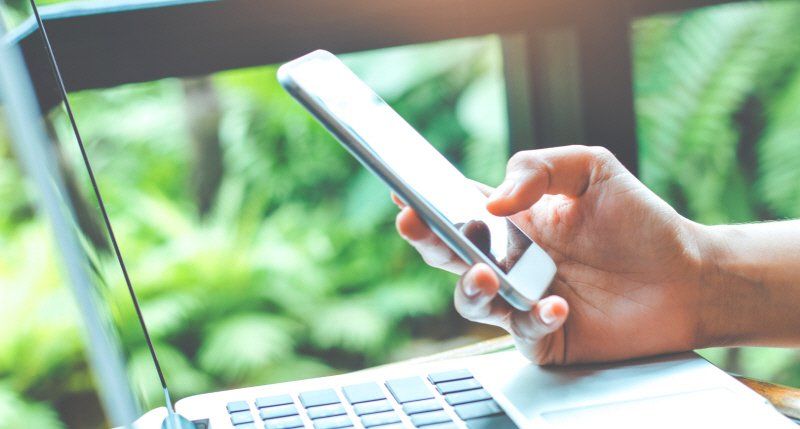 hand holding a mobile phone with a laptop