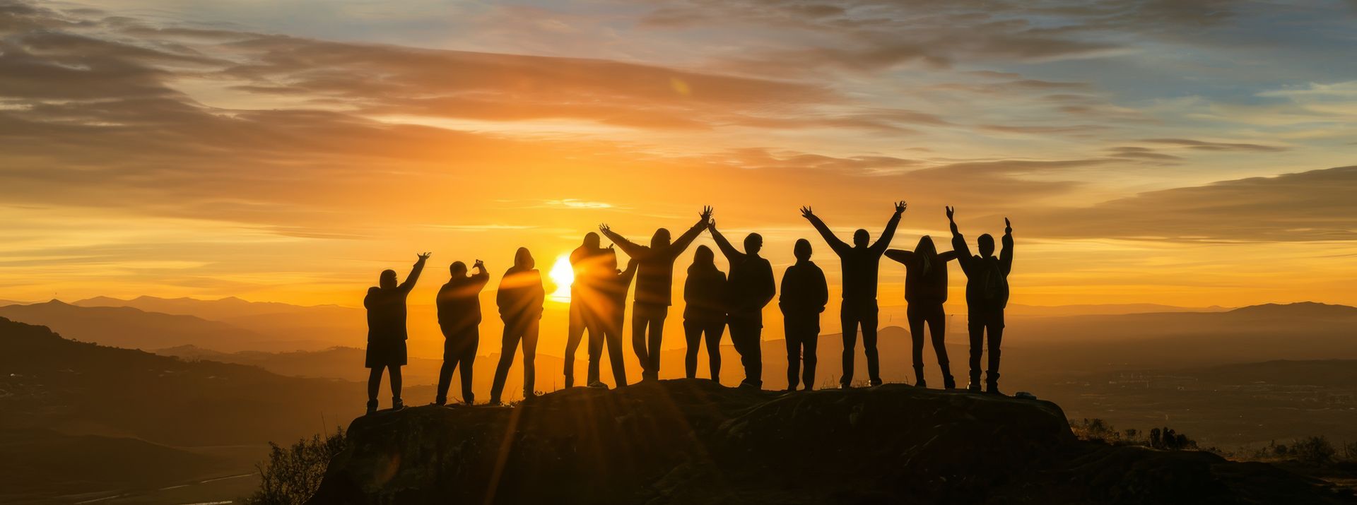 Silhouetted group standing on a hill at sunset, arms raised against a golden sky.
