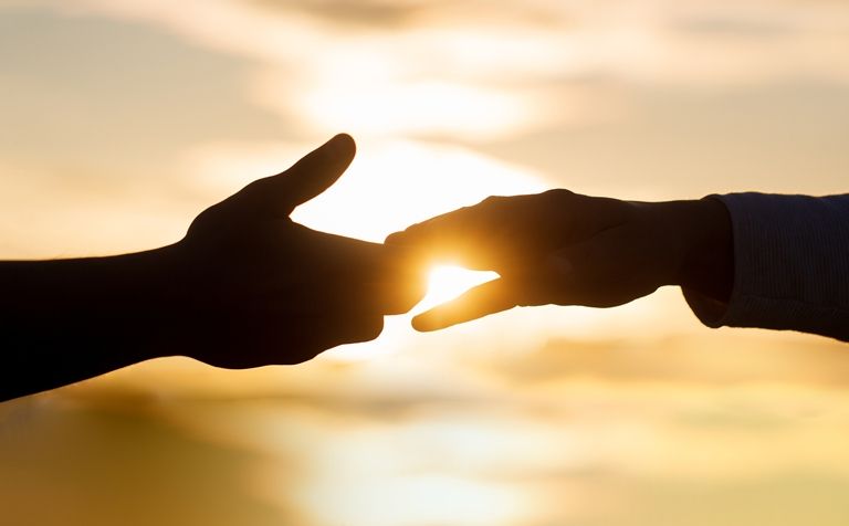 Two people are shaking hands in front of the sun at sunset.