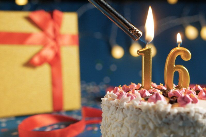 Image showing wrapped gift and birthday cake with numeric candles being lit showing 16