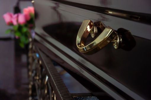 Gold handle on a shiny, dark wooden surface, with a blurred bouquet of pink roses in the background.