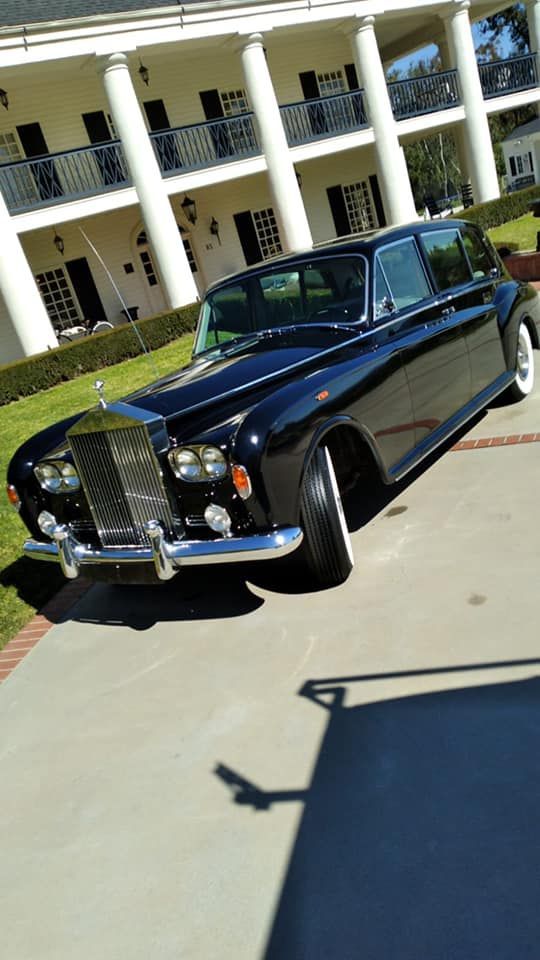 Black vintage sedan parked on a sunny driveway in front of a white building with columns
