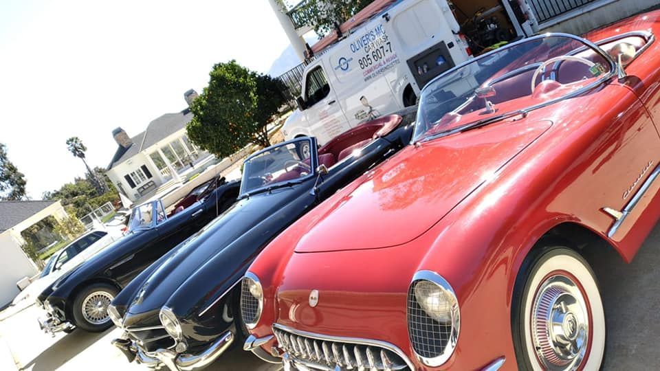 Red and navy vintage convertibles parked at a car show on a sunny street