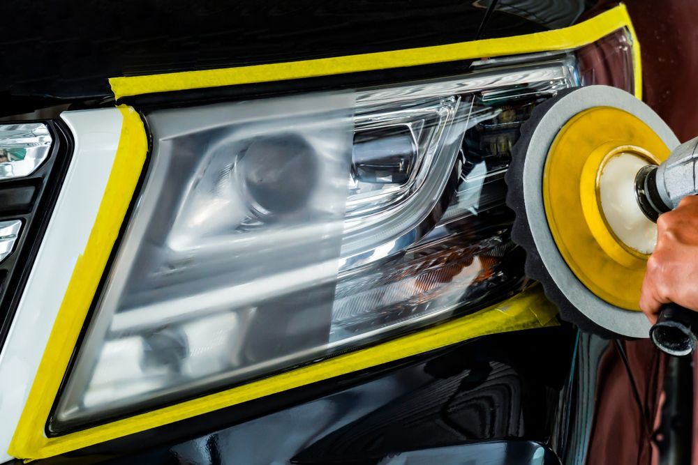 Person polishing a car headlight with a yellow buffer and black trim visible