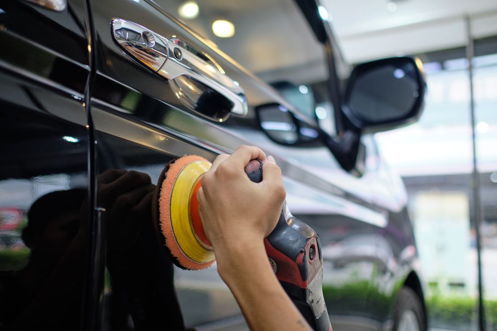 Hand polishing a black car with a red and yellow buffing pad in a garage
