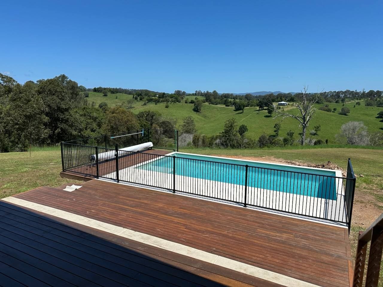 A Large Swimming Pool Surrounded By A Fence And A Wooden Deck — CJB Pools in Gympie, QLD