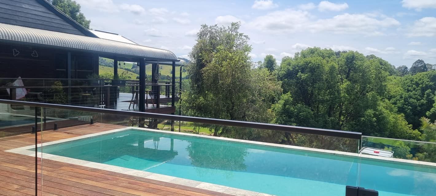 A Large Swimming Pool Is Surrounded By Trees And A House — CJB Pools in Gympie, QLD