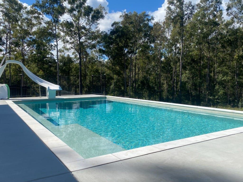 A large swimming pool with a slide and trees in the background — CJB Pools in Gympie, QLD