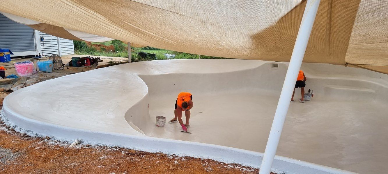 A Man Is Working On A Concrete Surface Under An Umbrella — CJB Pools in Gympie Southside, QLD