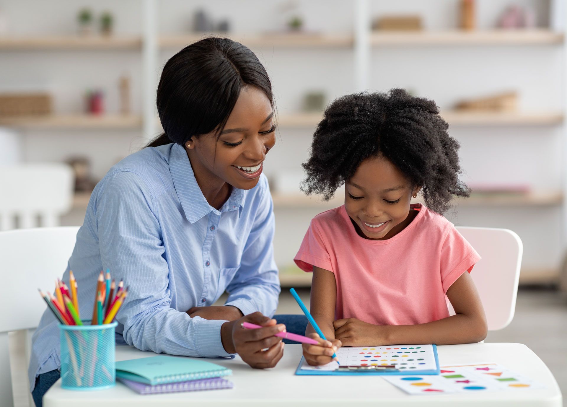 An adult and a child sitting at a desk, the adult pointing at the child's paper.