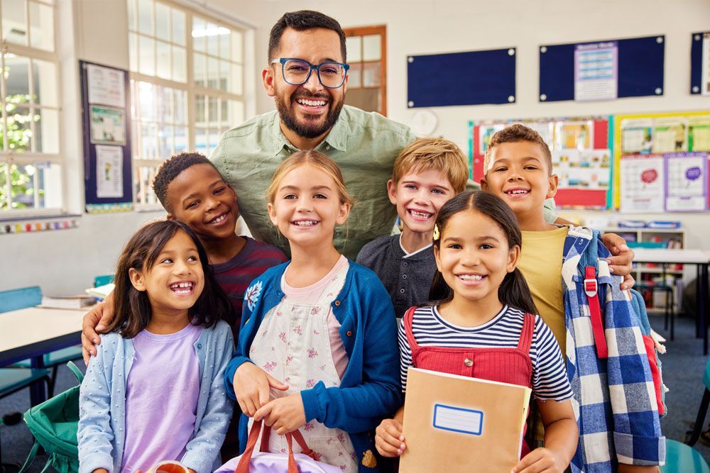 Smiling teacher with students in a classroom. They are happy and looking at the camera.