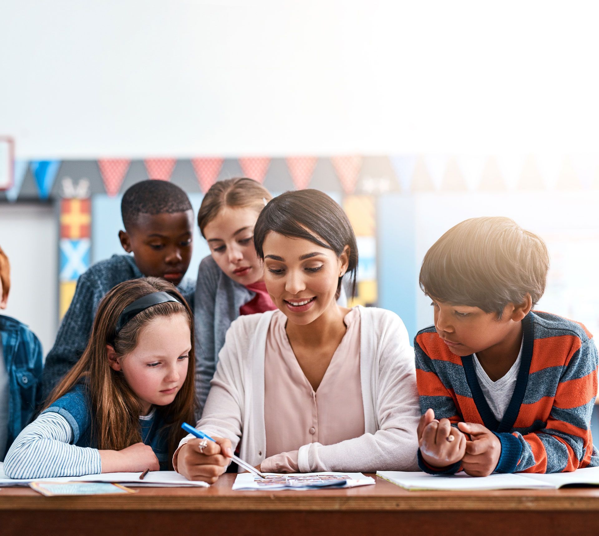 Teacher helping students with their work at a desk in a classroom.