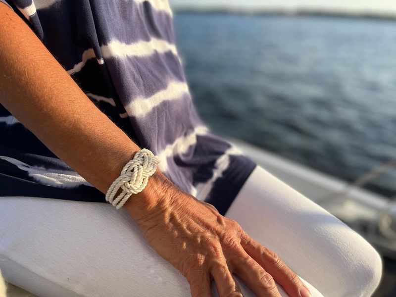 A woman wearing a bracelet is sitting on a boat near the water.