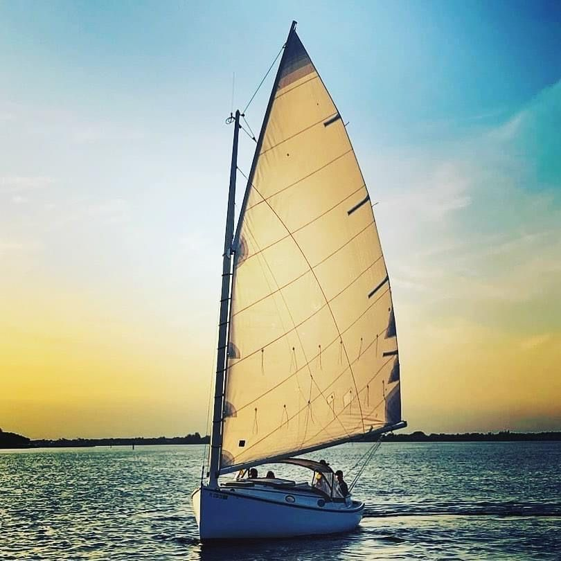 A sailboat is sailing on the water at sunset. Catboat Margot