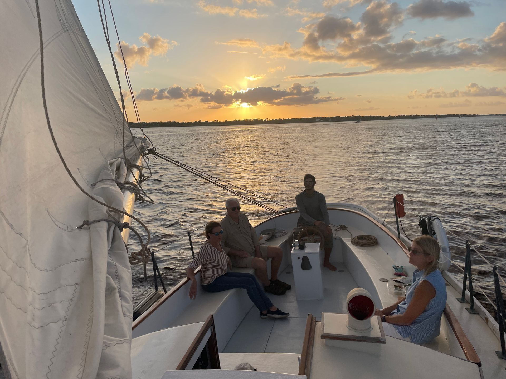 A group of people are sitting on a boat in the water at sunset. Sailing Adventures in Palm City