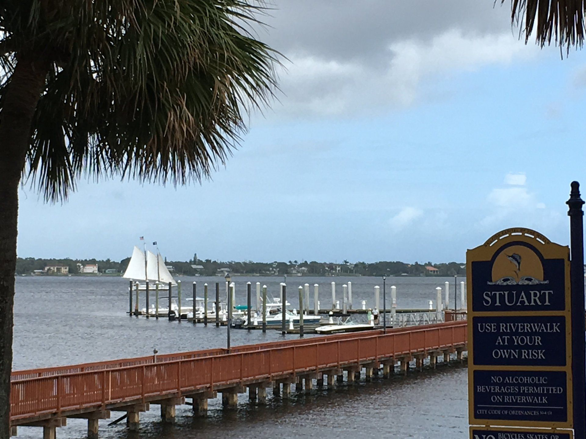 A sign that says stuart on it in front of a dock. Schooner Lily sails on the river from Downtown Stuart riverwalk Pier