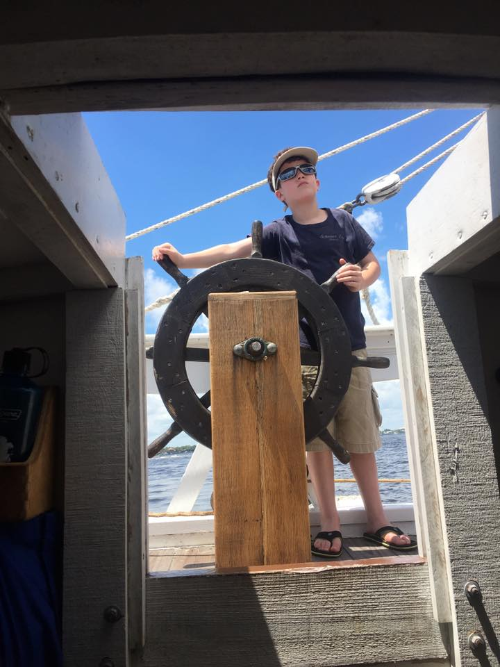 A young boy is standing at the steering wheel of a boat