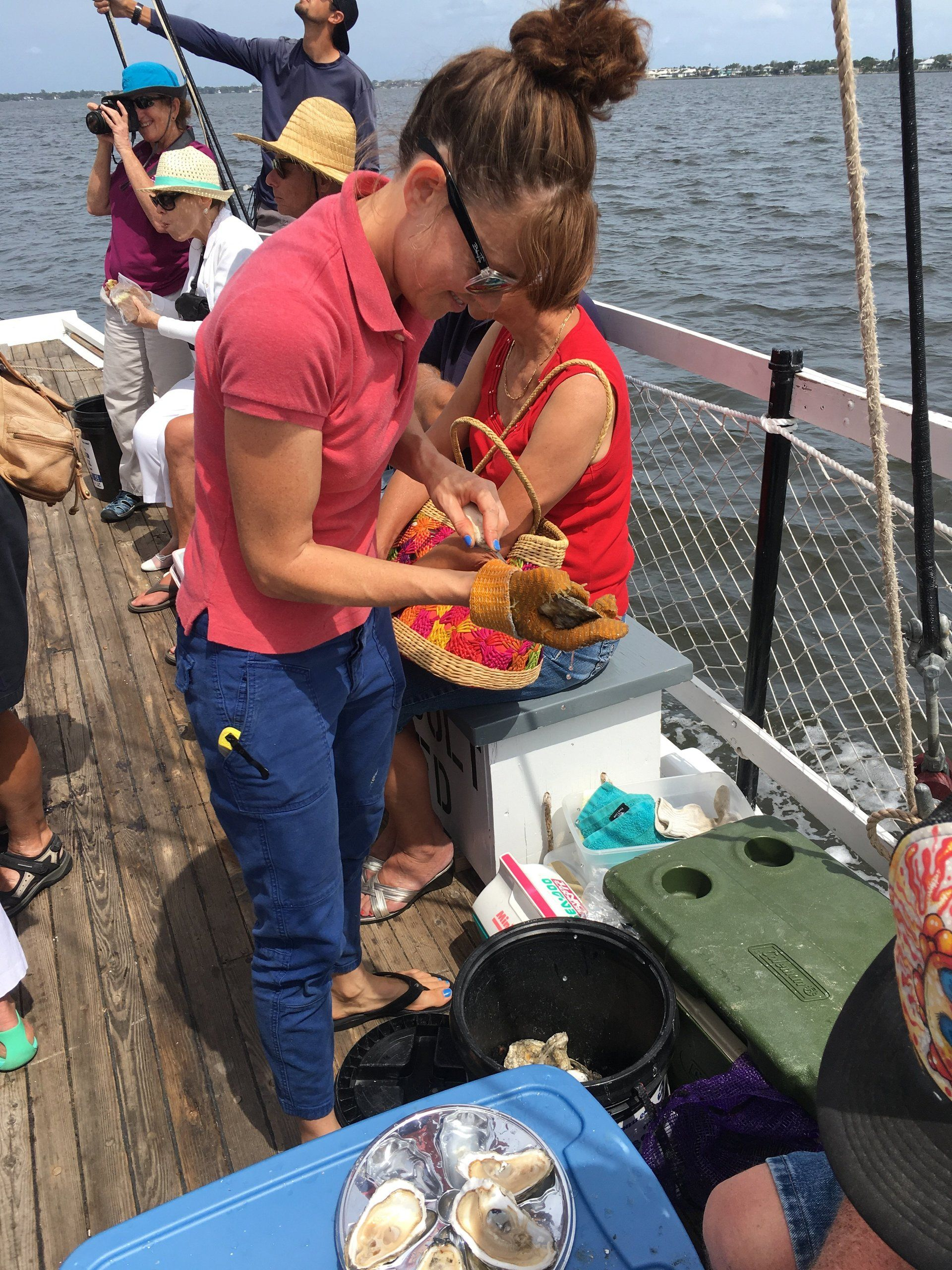 A group of people are standing on a boat eating food. Oyster cruise on the Schooner Lily in Stuart Florida