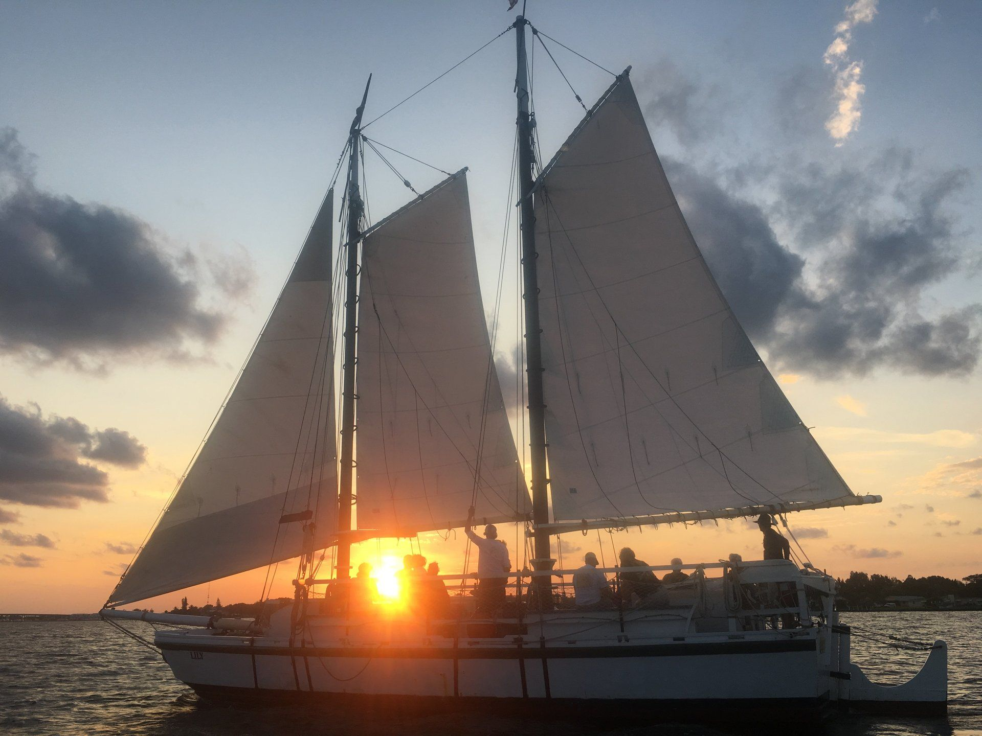 A sailboat in the water at sunset with the sun shining through the sails