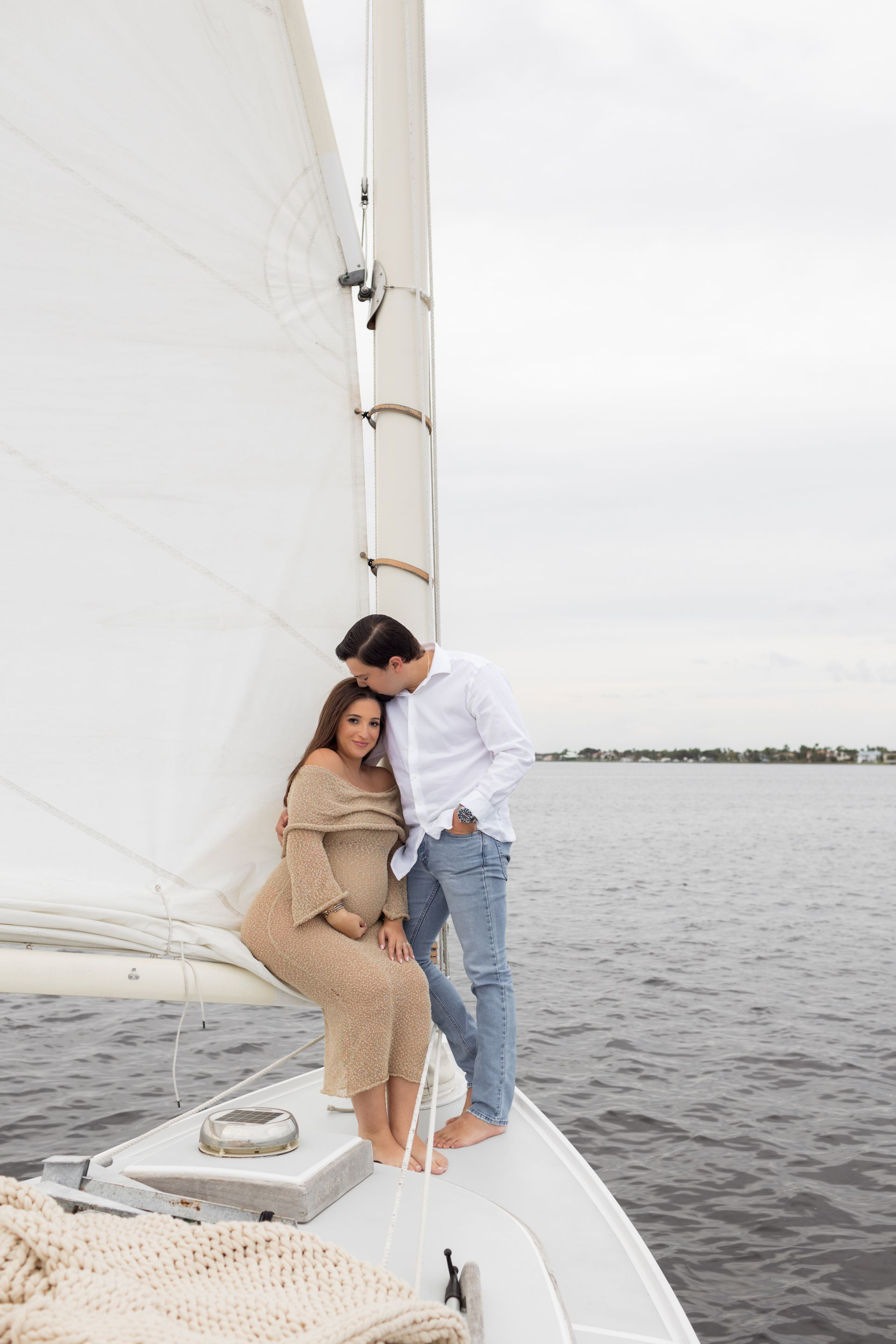 A man and a pregnant woman are sitting on the back of a sailboat.
