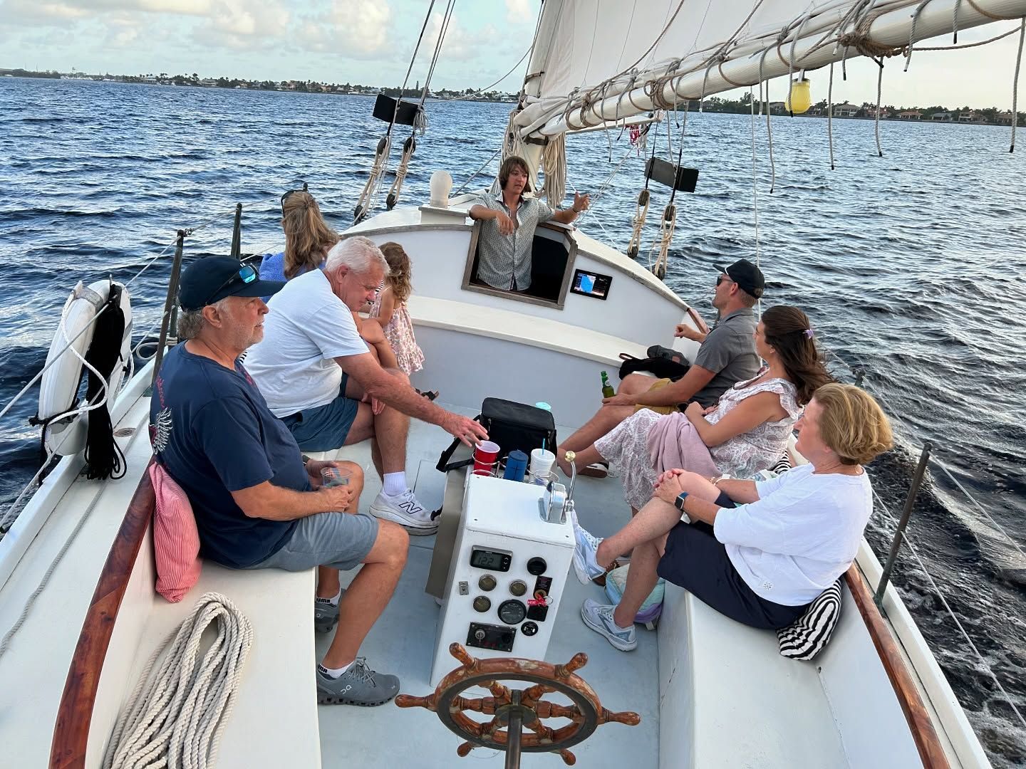 People sailing on a boat at dusk; one person steering, others relaxing and enjoying the ride.