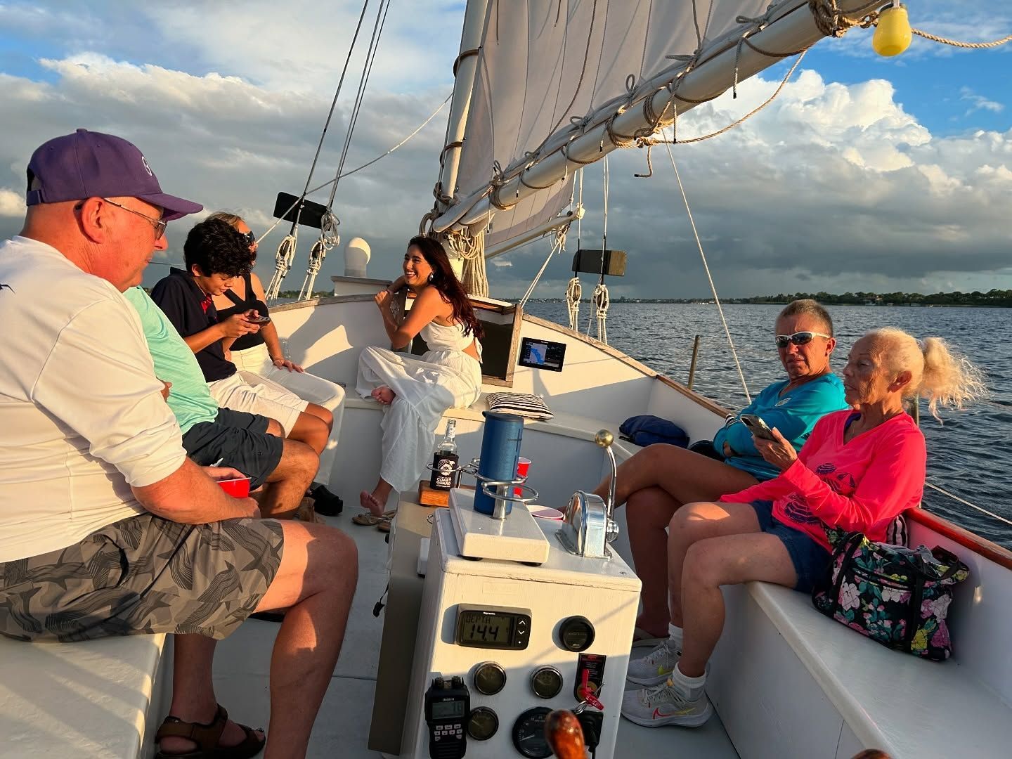 People on a sailboat deck at sunset; calm water, cloudy sky.