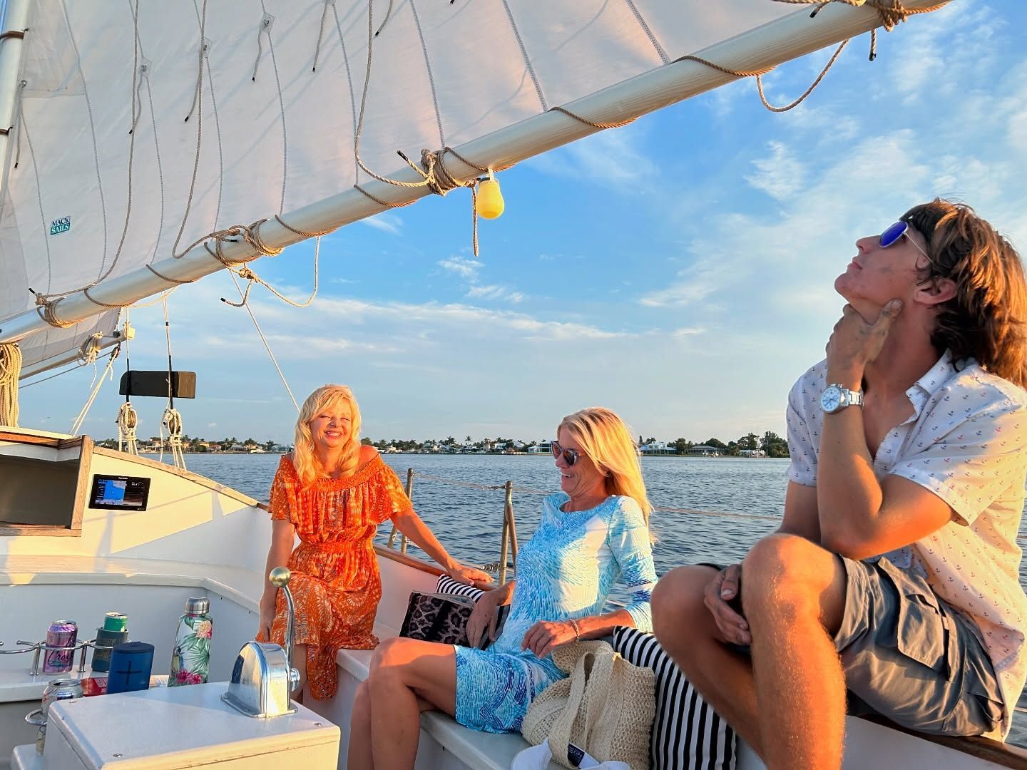 People on a sailboat, enjoying the sunset. Two women and a man, looking up.