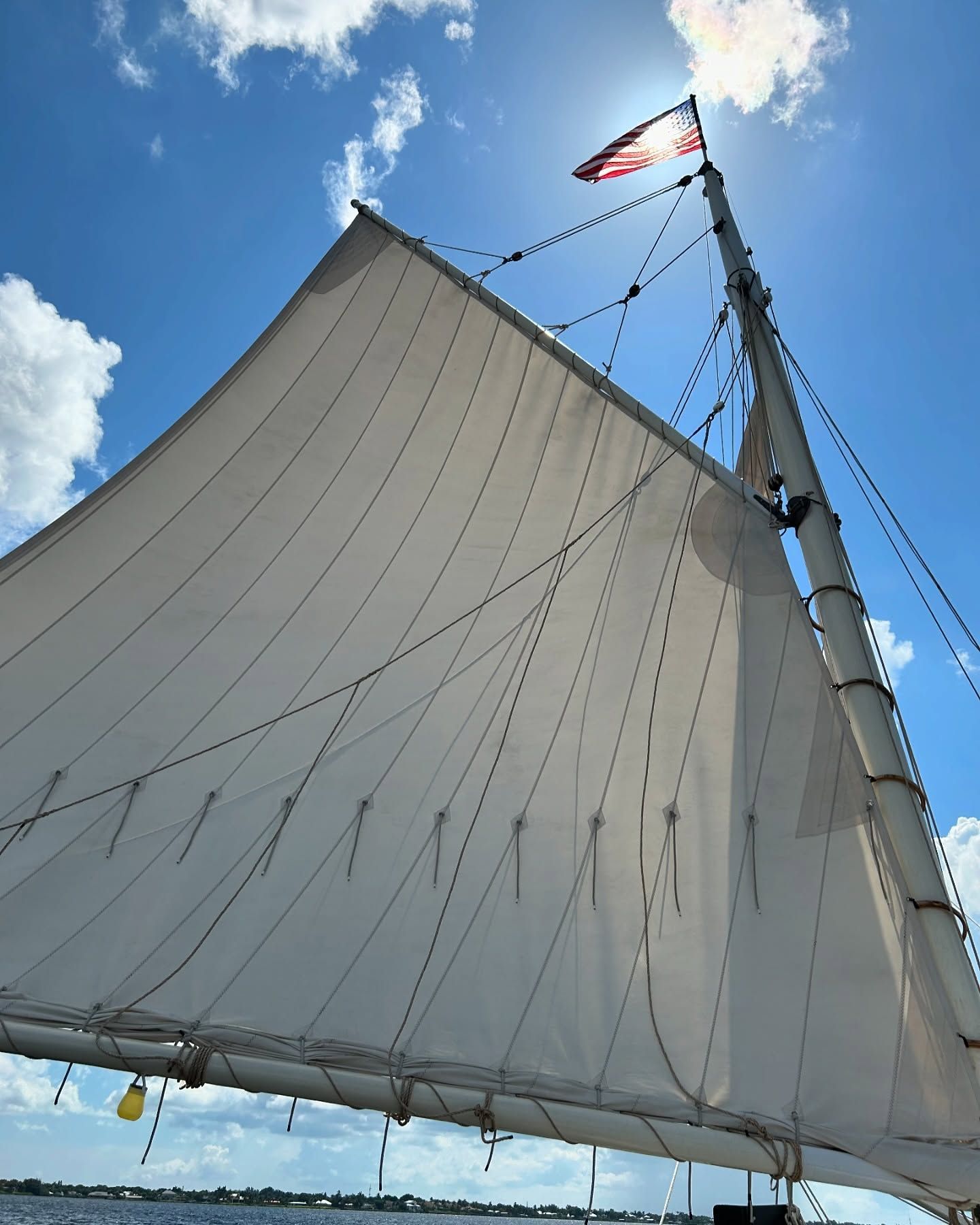 Sailboat with billowing white sail against a bright blue sky. American flag waves at the mast.