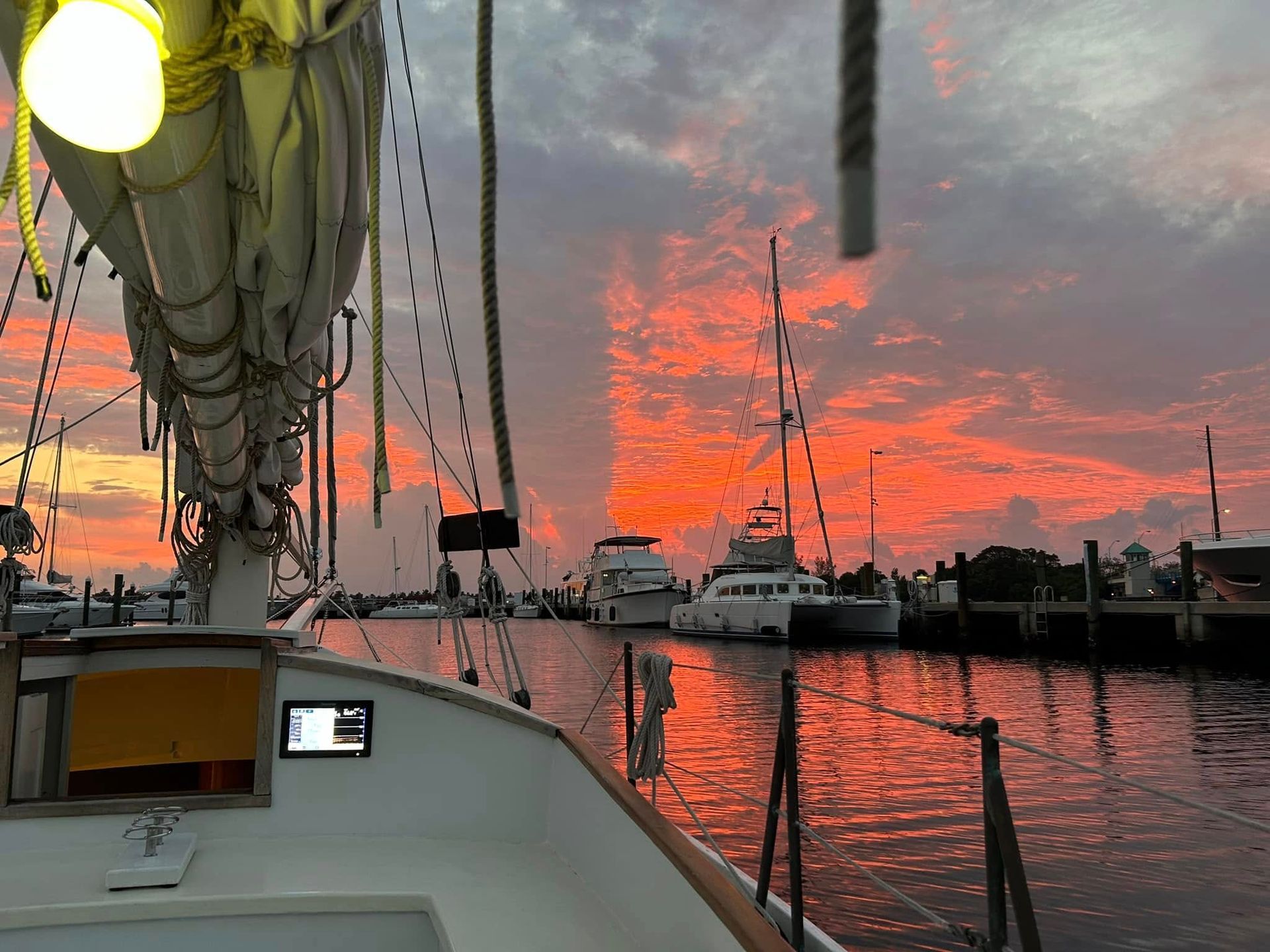 Sunset over boats in a marina, from the deck of a sailboat. Vivid red and orange sky.