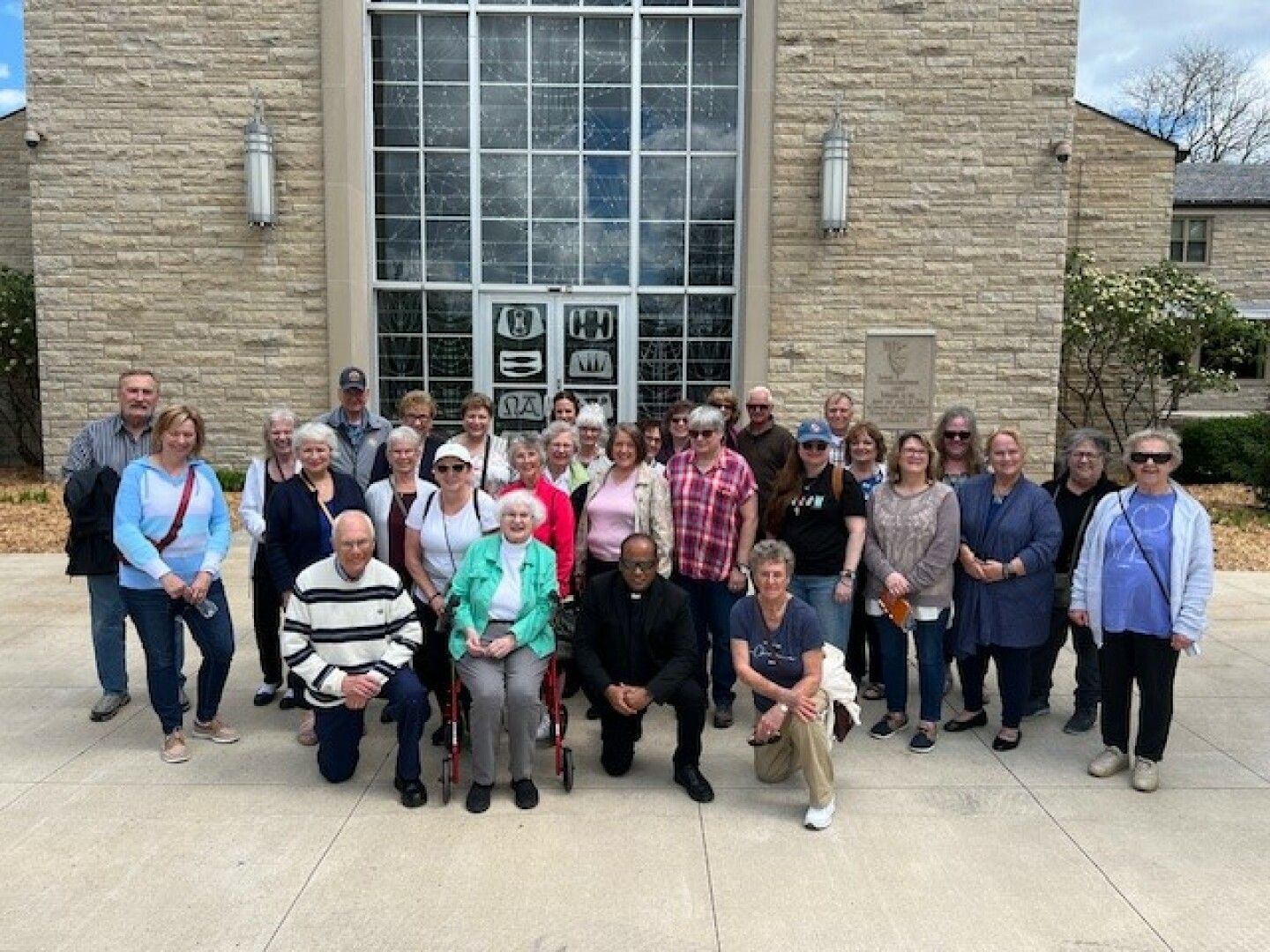 A group of diverse adults posing in front of a stone building with large windows and emblem designs.