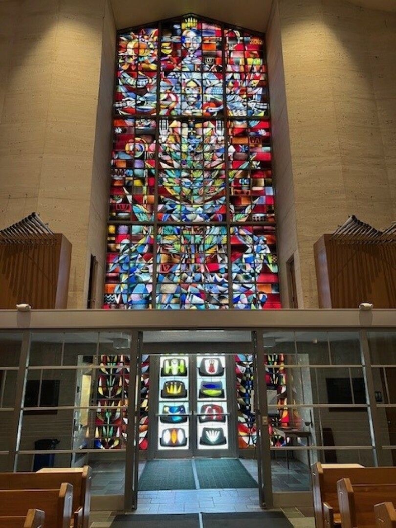 Stained glass window in a church, depicting vibrant abstract patterns with reds, blues, and yellows. 