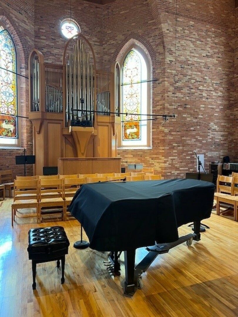 A grand piano covered with a black cloth sits in a brick-walled chapel. 
