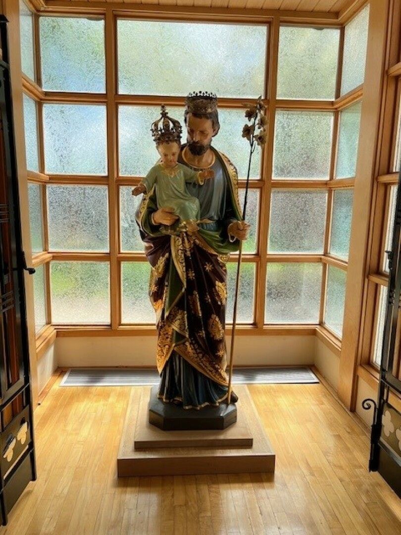 A bearded statue holds a child, both with crowns, set in front of a multi-panel window. 