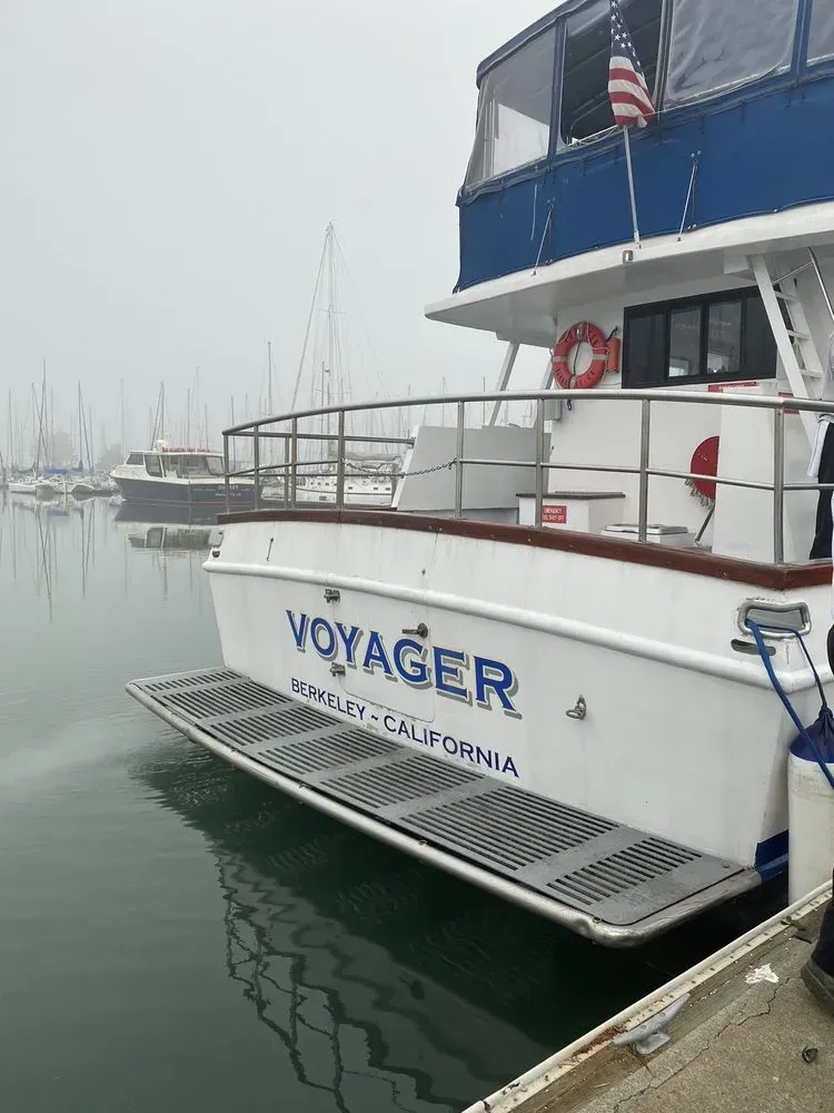 White Voyager boat docked in water; California, USA. Blue accents, cloudy day.